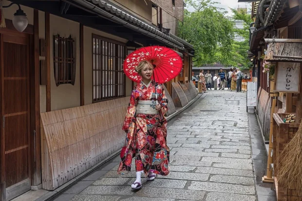 Portrait photograph of a walking woman wearing a red yukata with an oil-paper umbrella, in Gion, Kyoto, Japan